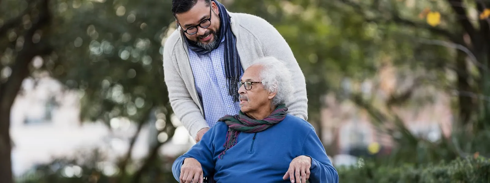 A caregiver talks with his father while pushing his wheelchair, confident that caregiver life insurance will protect his father’s care if he passes away.