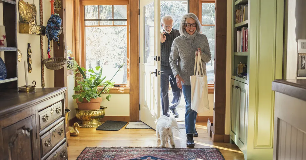 A senior couple walking into their home, being greeted by their dog. 