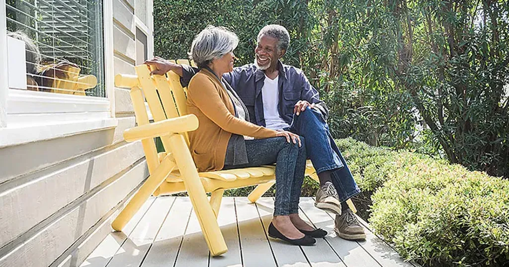 Senior couple sitting on a back porch, smiling and looking at each other. 