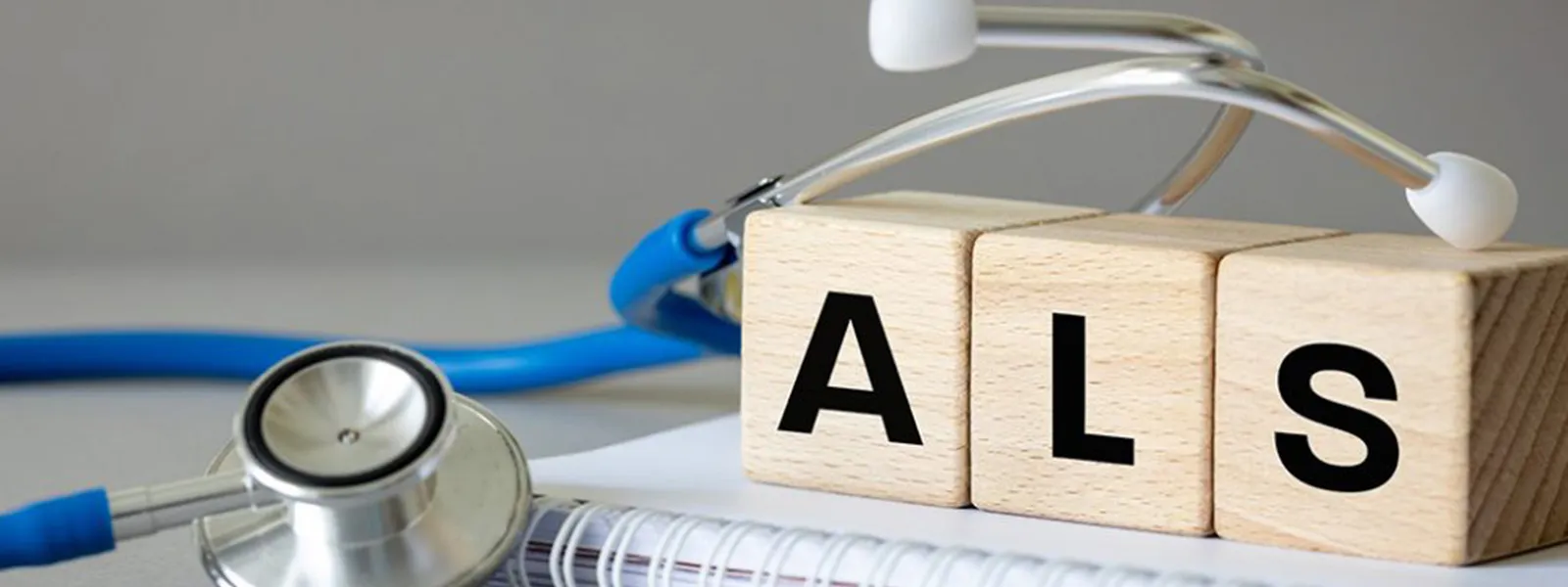 A stethoscope next to a notebook and blocks with the letters ALS on them.