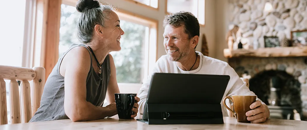 Husband and wife laughing while sharing a coffee in front of their tablet