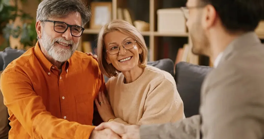 reitred couple smiling together on a couch with a man in the foreground