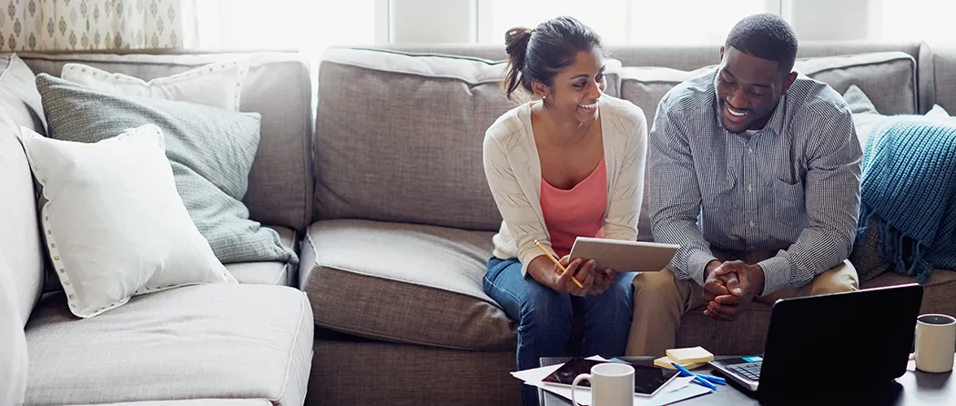 Couple sitting on a couch smiling while going over paperwork