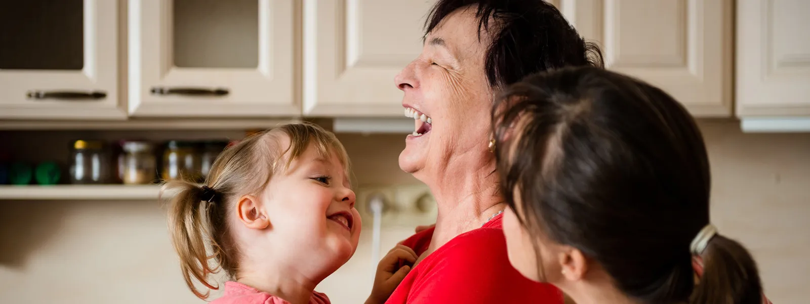 A grandmother with her daughter and grand daughter laughing in the kitchen.
