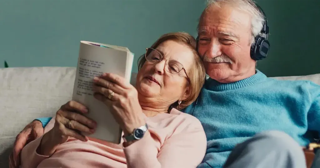 Senior couple sitting together on a couch, reading a book together. 