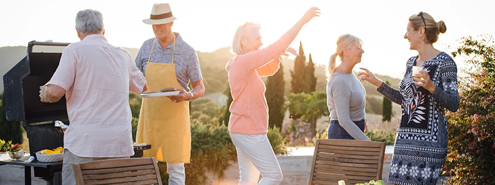 A group of senior people are having a BBQ, they are cooking/preparing food together.