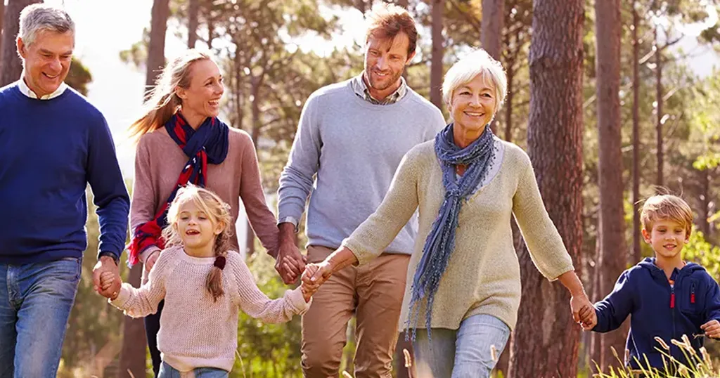 A multigenerational family holding hands and walking together in the woods. 