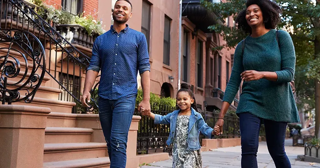Man and woman holding hands with a little girl, walking down a city block.