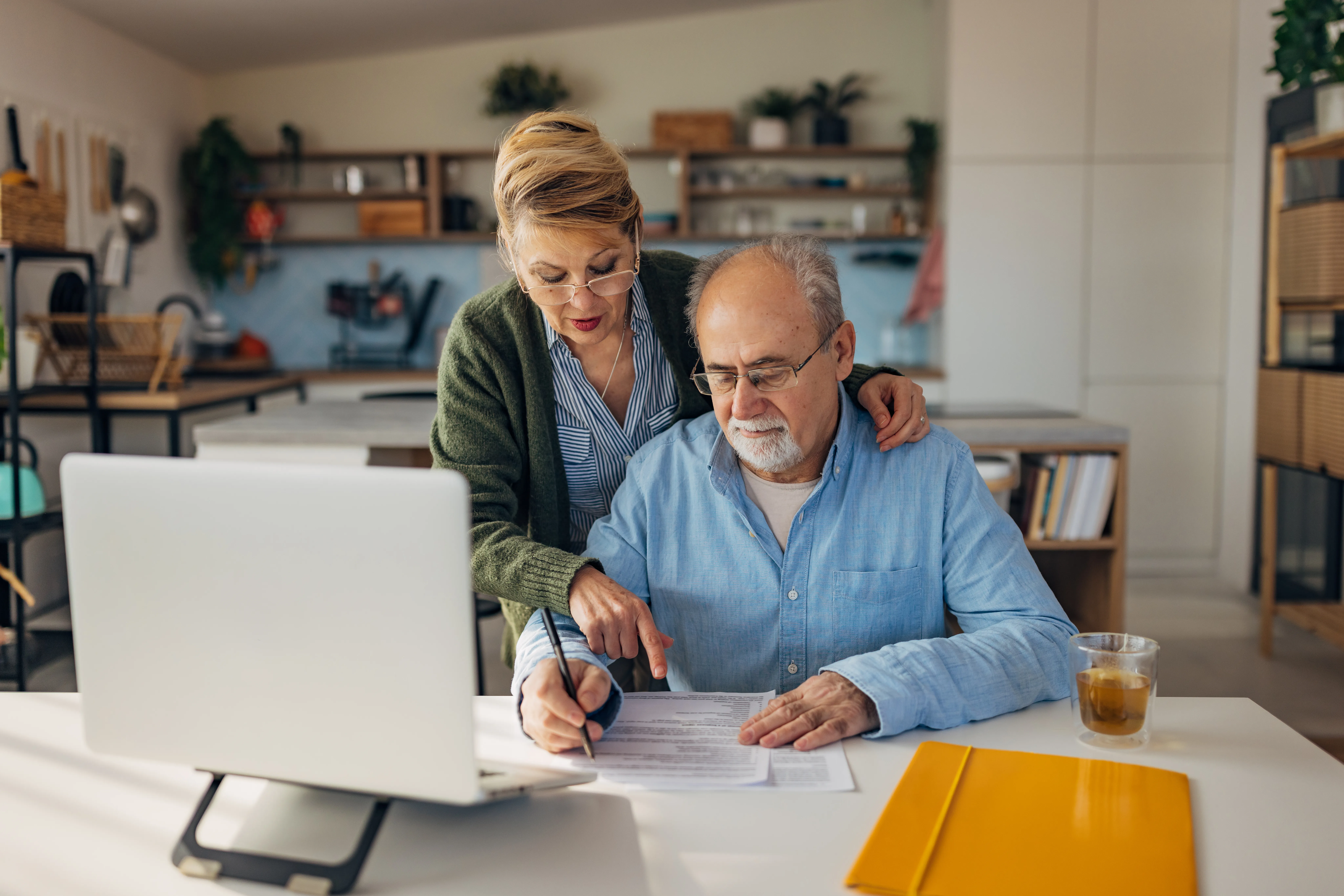 Couple in their 50s looking over a piece of paper at their laptop. 