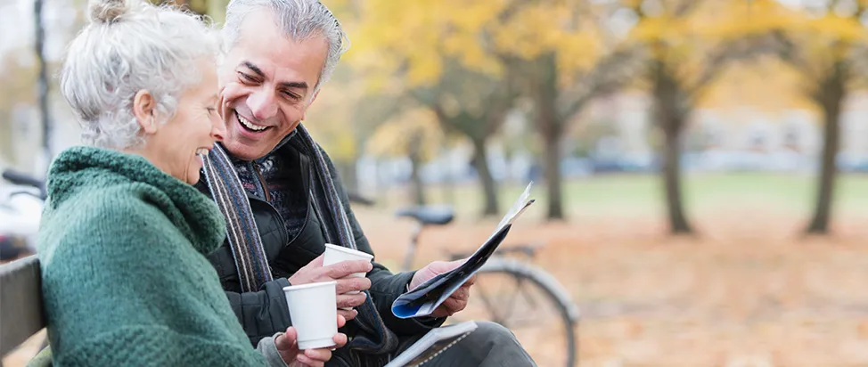 Senior couple sitting on a bench drinking coffee at the park