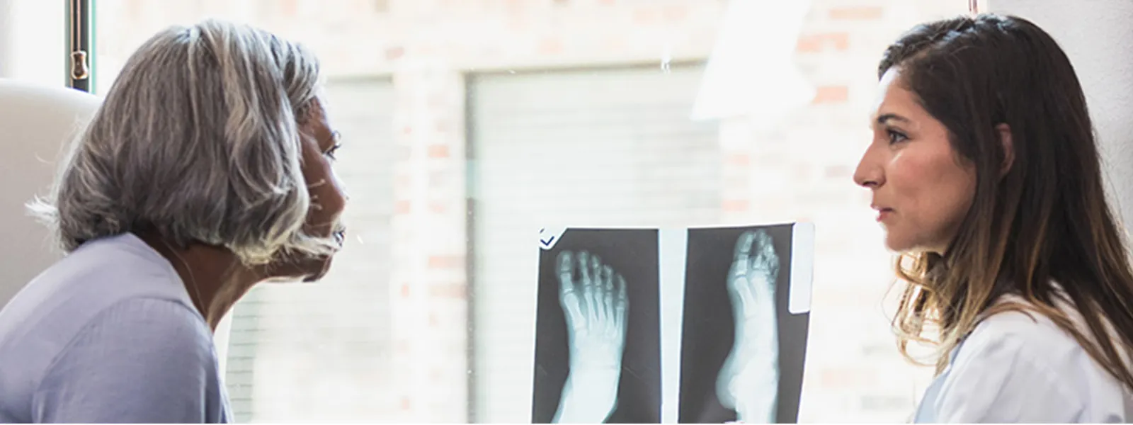 A female orthopedic doctor shows a senior female patient an x-ray of the patient's foot.