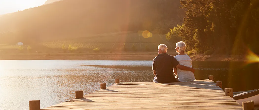 Elderly couple sitting on a dock at sunset