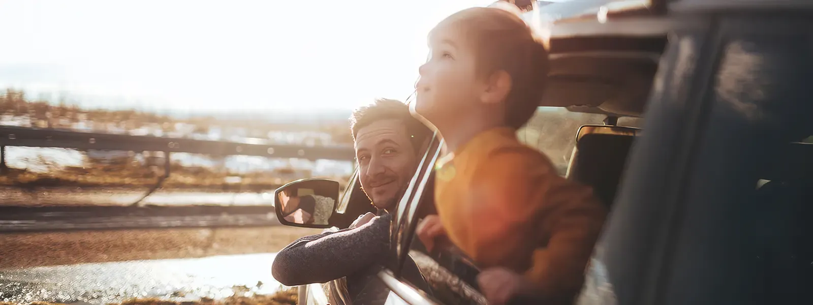 Hero image of a man and his son looking out of the car window into the sky