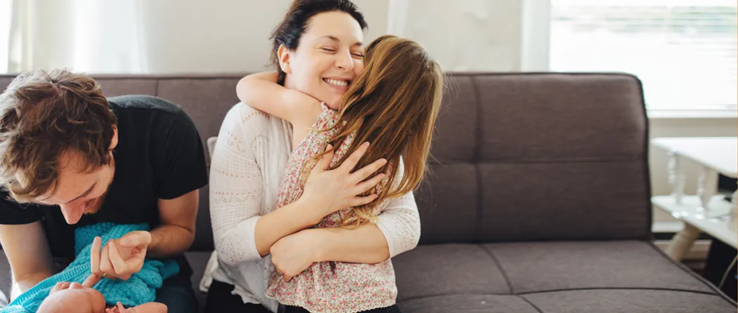 Mom hugging daughter while dad plays with baby