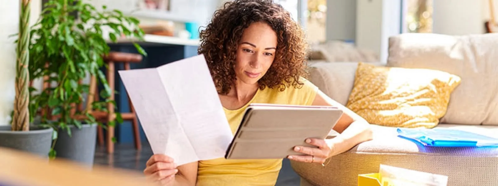 Woman sitting on the floor comparing paperwork to whats on her tablet
