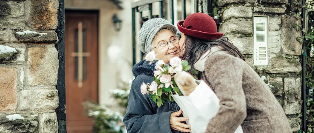 Daughter kissing her elderly mother on the cheek and giving her flowers