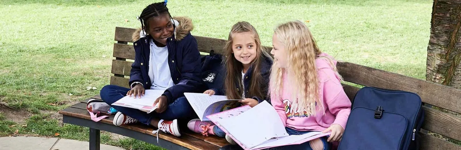 Children sitting on a wooden bench with backpack and notebook