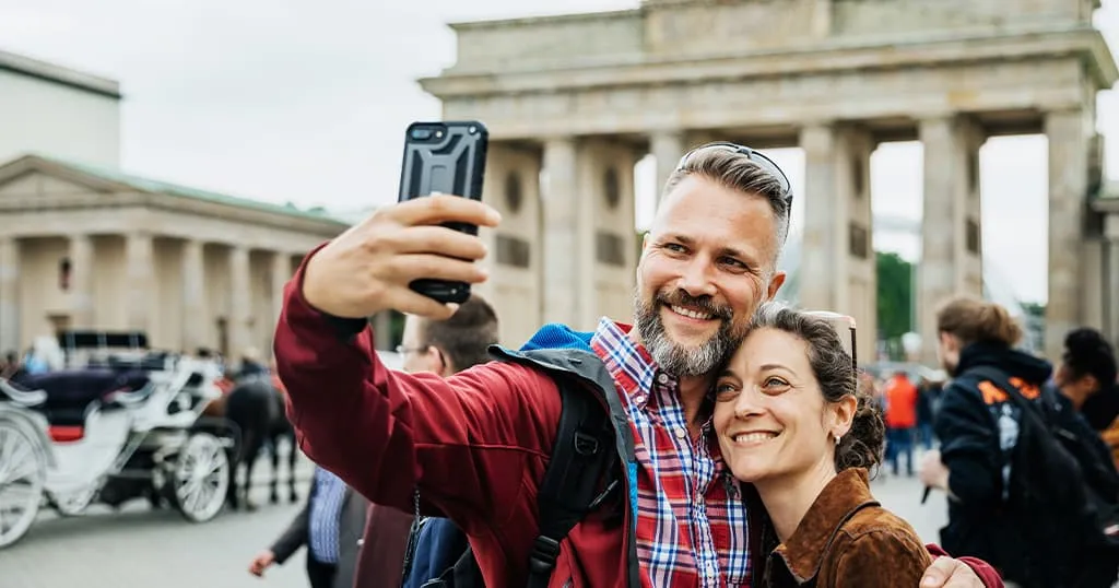 Tourist couple in their 40s posing in front of Greek ruins taking a selfie.