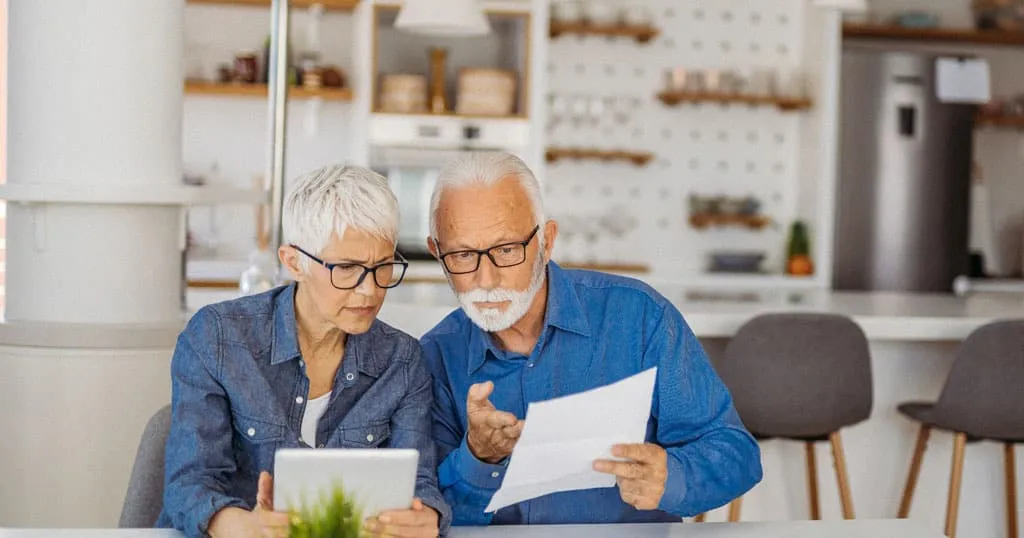 Older adult couple sitting in a kitchen looking at papers