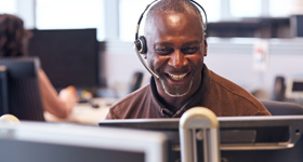 man with a headset smiling while working on his computer