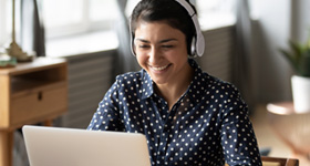 a woman with headphones on smiling while working on her laptop