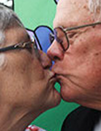 Jack and Sherry Hinkle kiss as they stand in front of a colorfully painted wall outdoors.