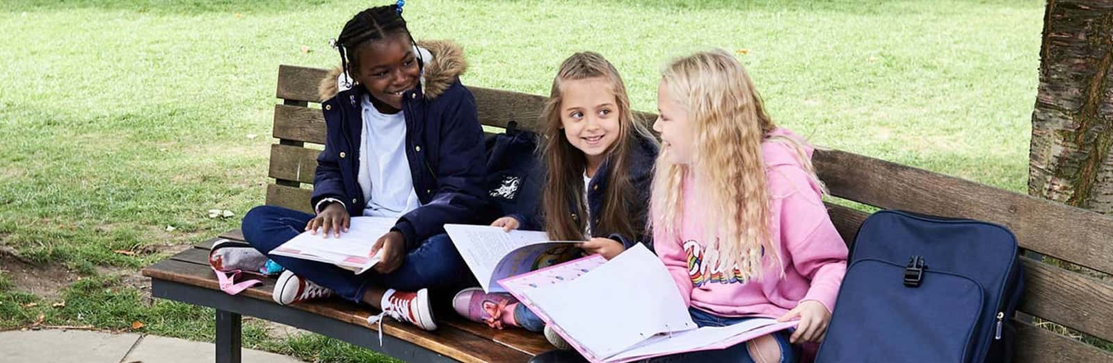 Children sitting on a wooden bench with backpack and notebook