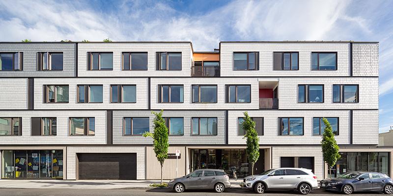 A view of the front of the PDX Commons senior cohousing community. It's a white apartment-style building filled with windows.