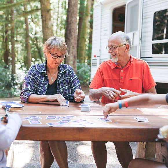 a woman and man playing cards outside at a table